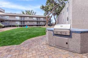 A brick patio with a built-in grill and apartment buildings in the background.