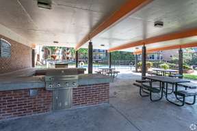 A covered picnic area with a grill and picnic tables.
