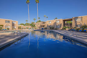 A swimming pool with a building and palm trees in the background.