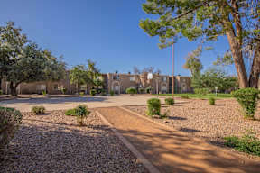 A courtyard with a building in the background and a gravel path leading to a door.