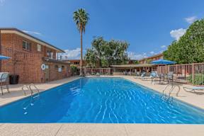 A large blue swimming pool surrounded by a fence and chairs.