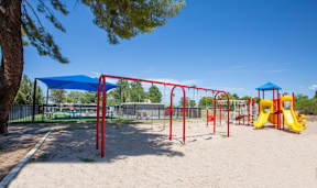 A playground with a red and yellow slide, a blue canopy, and a yellow sandbox.