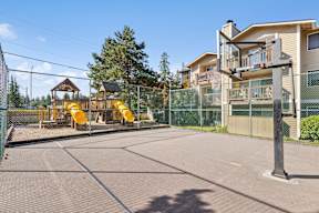 A playground with a yellow slide and a basketball hoop.