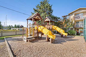 A playground with a yellow slide and a wooden structure.