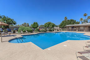 A large swimming pool surrounded by a concrete patio and lounge chairs.