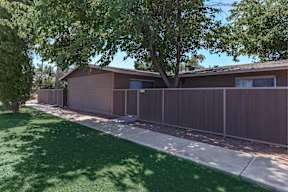 A brown house with a white fence and a tree in front.