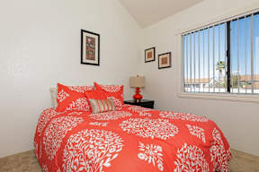 A bed with a red and white comforter is in the foreground of a room with a window.