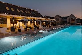 A swimming pool in front of a building with a sun lounger.