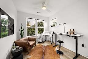 A room with a brown leather couch, a black stool, a white table, and a brown rug.