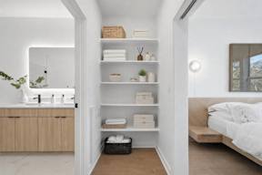 A bathroom with a sink, mirror, and shelves with towels and plants.