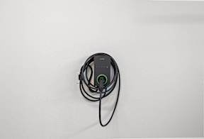 A black device with a green light is plugged into a white surface.