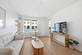 A living room with a white couch, a wooden coffee table, and a television on a wooden stand.