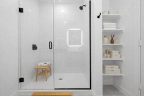 A white bathroom with a glass shower door and a wooden stool.