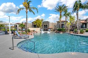 A pool surrounded by palm trees and a building in the background.