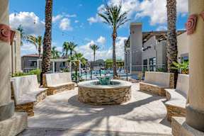 A courtyard with a fountain surrounded by palm trees and concrete pillars.