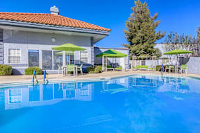 A swimming pool in front of a house with a red roof.