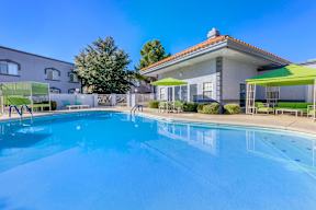 A swimming pool in front of a house with a green umbrella.