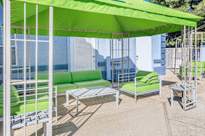 A patio with a green umbrella and matching chairs.