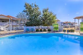 A large swimming pool surrounded by a white fence and green chairs.