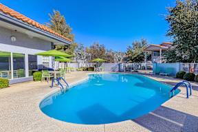 A swimming pool with a blue tinted water and a green umbrella.