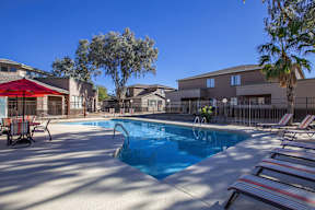 A pool surrounded by lounge chairs and a red umbrella.