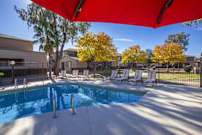 A pool with a red canopy and lounge chairs.