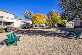 A park with benches and trees in front of apartment buildings.