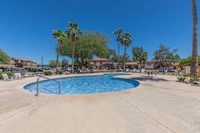 A pool surrounded by palm trees and lounge chairs.
