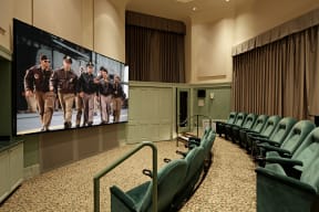 a large screen with a group of men on it in a large room with green chairs