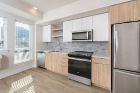 Blonde design package kitchen with two tone cabinets, wood-style plank flooring, and stainless steel appliances