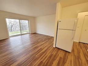 an empty living room with a refrigerator and a window