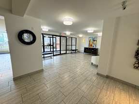 A hallway with a clock on the wall and a bookshelf in the background.