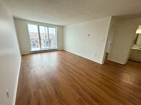 Empty room with wooden flooring and large windows.
