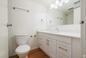 A white toilet is in a small bathroom with a white sink and a mirror.