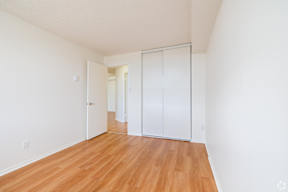 A room with white walls and wooden flooring with a white door and a white wardrobe.