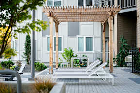 A wooden pergola is in front of a white building.at Copestone Apartments, Garden City, 59808