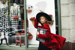 a woman in a red dress holding a magazine standing in front of a store window