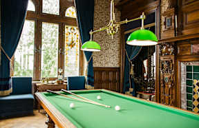A pool table in a room with a green cloth and a green lamp.
