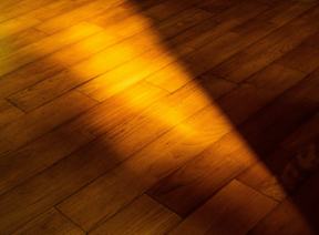 A shadow of a person is cast on a wooden floor.