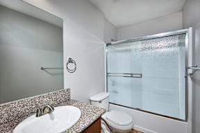 A bathroom with a toilet, sink, mirror, and shower.