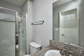 A bathroom with a toilet, sink, mirror, and shower.