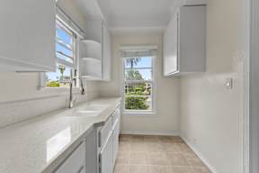 A kitchen with white cabinets and a window overlooking a tree.