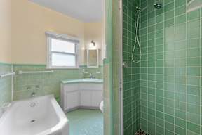A bathroom with a green tiled shower and a white bathtub.