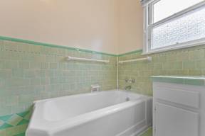 A white bathtub sits in a bathroom with green tiles.