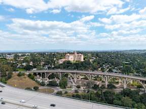 A bridge over a highway with cars driving on it and a city in the background.