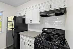 A black refrigerator is in a kitchen with white cabinets and a black stove.