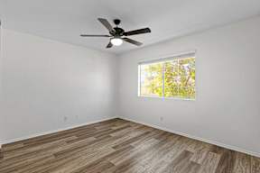 A room with a ceiling fan and a window showing trees outside.