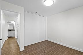 A white room with wood flooring and a mirror on the wall.
