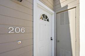 A white door with a window in the middle is on the side of a house with the number 206 on the wall.
