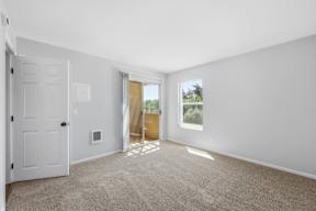 A room with a white door, carpeted floor, and a window with a view of the outdoors.